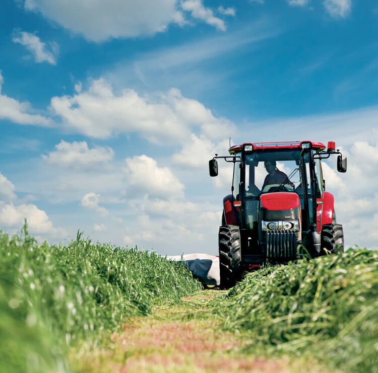 Red Case IH tractor working in a green field under a blue sky
